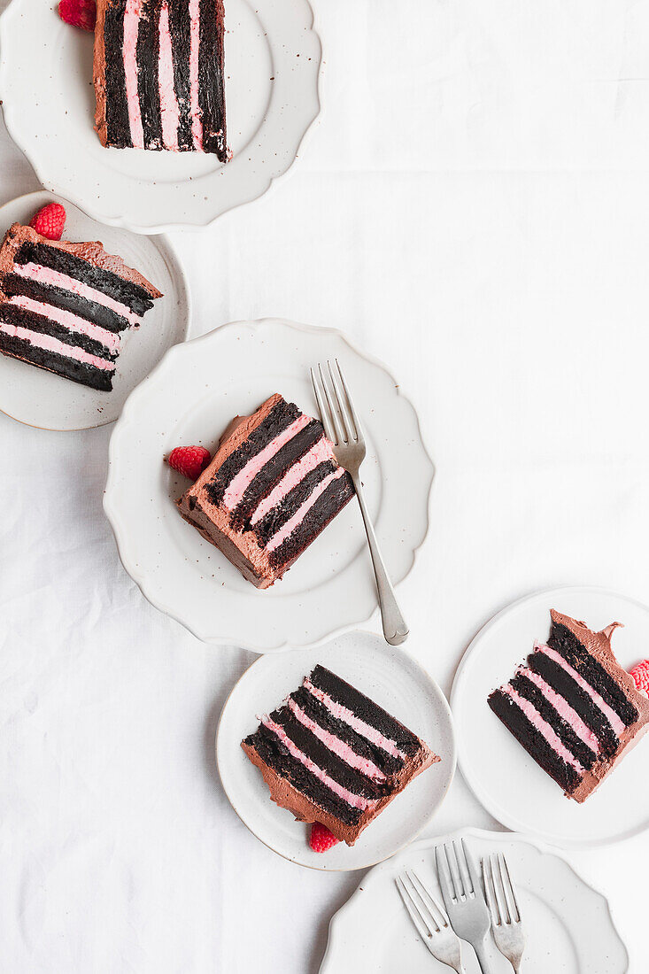 Multiple slices of raspberry and chocolate cake, on plates with forks