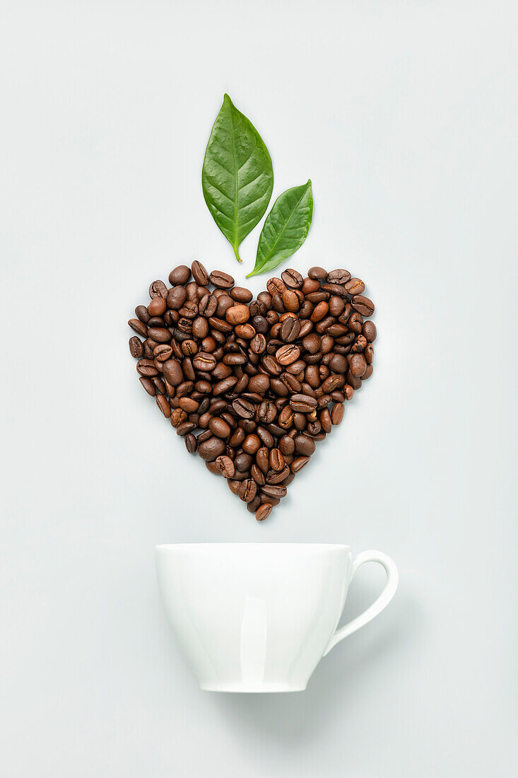 White ceramic coffee cup and coffee beans in shape of heart on white background, flat lay