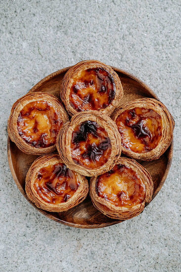 Six Pasteis de nata (small traditional Portuguese cake) placed on a wooden plate