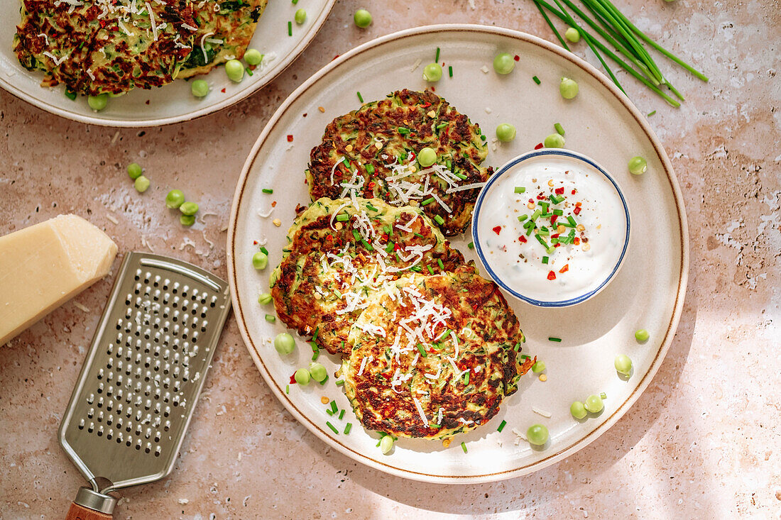 Zucchini pancake, peas, chives, grated parmesan, cheese grinder, pot of spicy cream, in white plate
