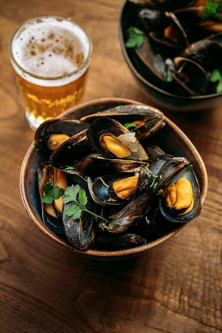 Close up of a bowl of mussel marinieres with parsley, and beer on wooden table