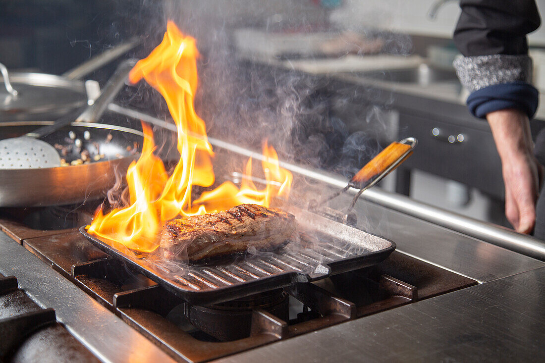 Crop anonymous male chef grilling meat on pan with flame while cooking in kitchen of restaurant