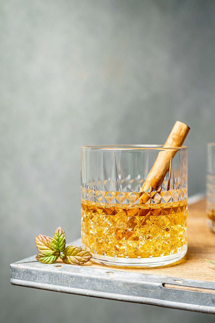 Crystal glass with whiskey served with stick of spicy cinnamon placed near leaf on corner of table