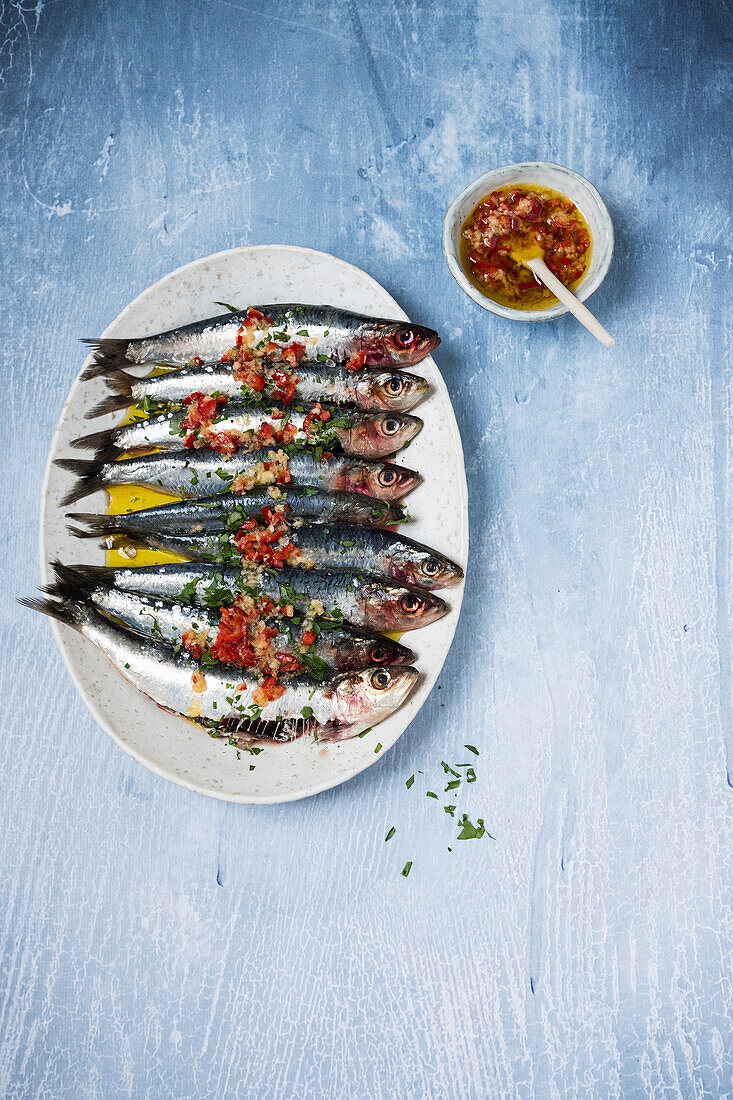 Tasty sardines garnished with spicy oil sauce served on plate on blue table