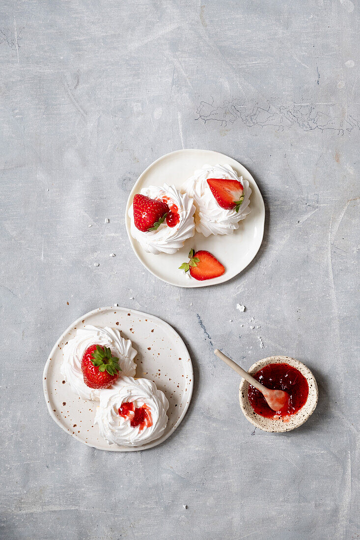 White sweet meringue with strawberries and tasty jam served on plate on gray marble table