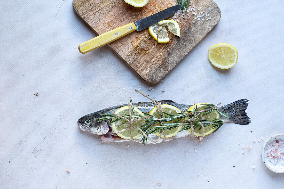 Fresh raw trout with lemon slices and rosemary twigs andcutting board on gray background