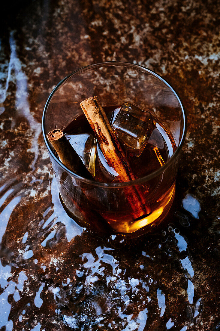 Glas Whiskey mit Zimstangen auf nassem Untergrund