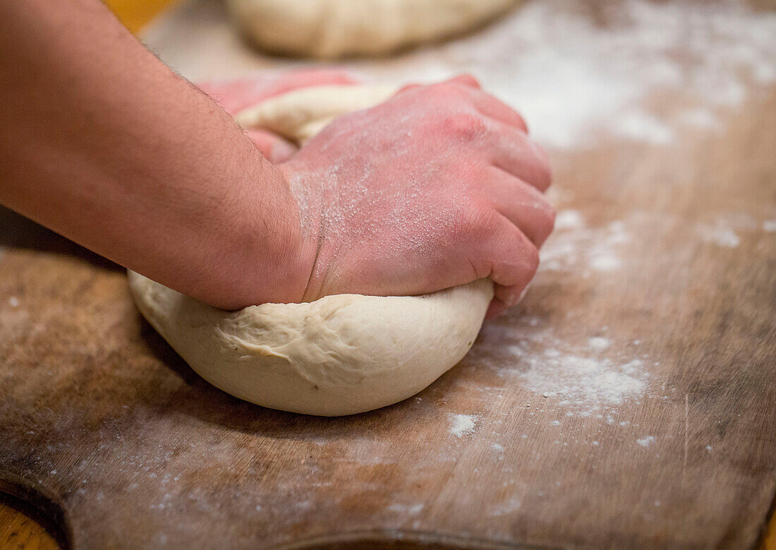 Hands of crop anonymous baker kneading raw soft dough on cutting board while preparing for baking bread in light bakery