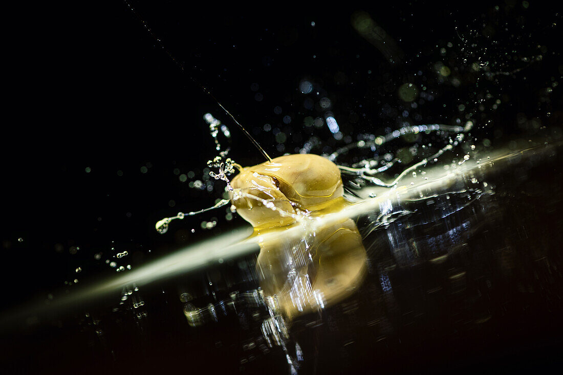 Healthy green oval olive in splashing oil placed on dark table