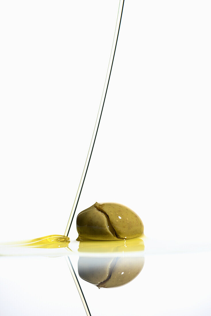 Grüne Olive und Olivenölstrahl vor weißem Hintergrund