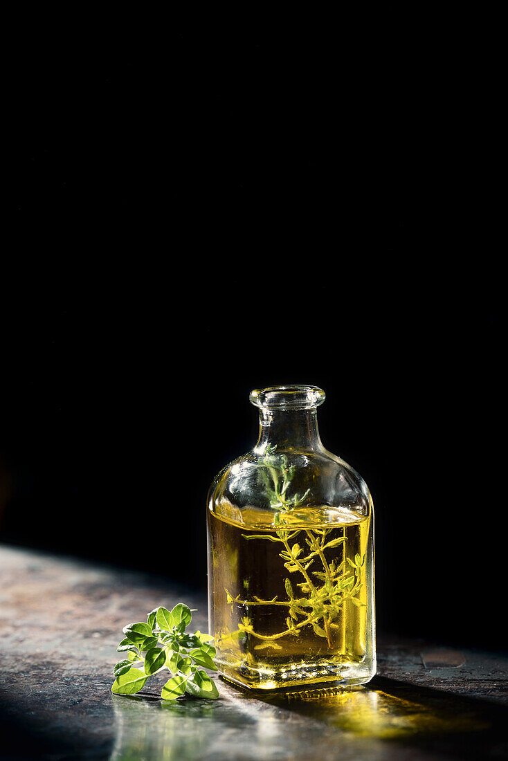 Olivenöl mit Thymianzweig in Glasflasche vor schwarzem Hintergrund