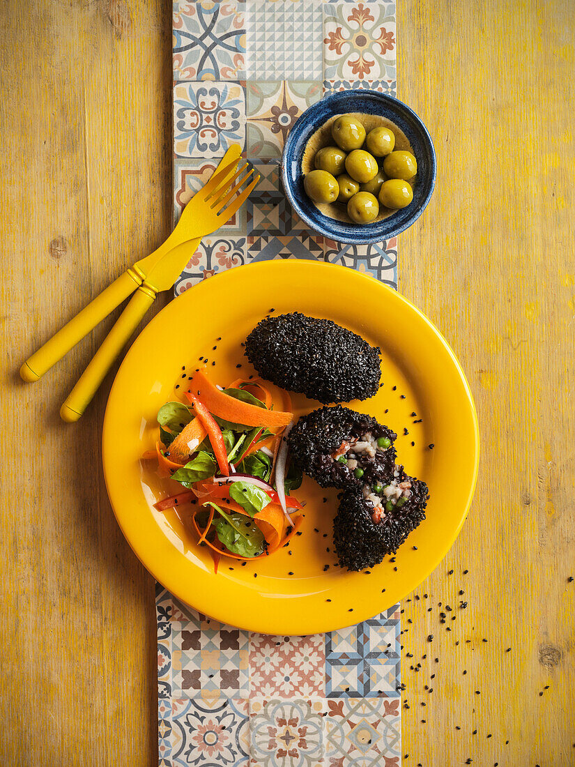 Arancini in a black sesame seed coating filled with rice, fish and vegetables