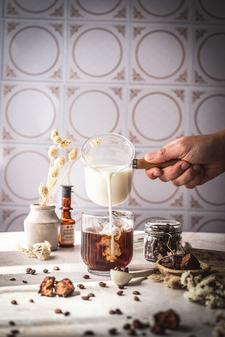 Making the iced coffee: Pouring milk into a glass with coffee and ice cubes