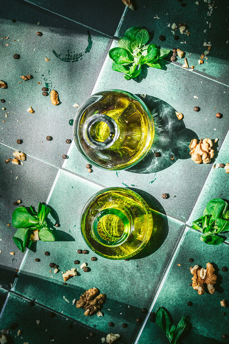 Two bottles of olive oil on a green tile background