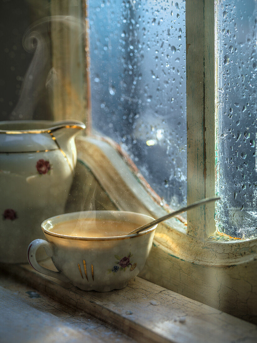 A steaming cup of coffee in front of a window