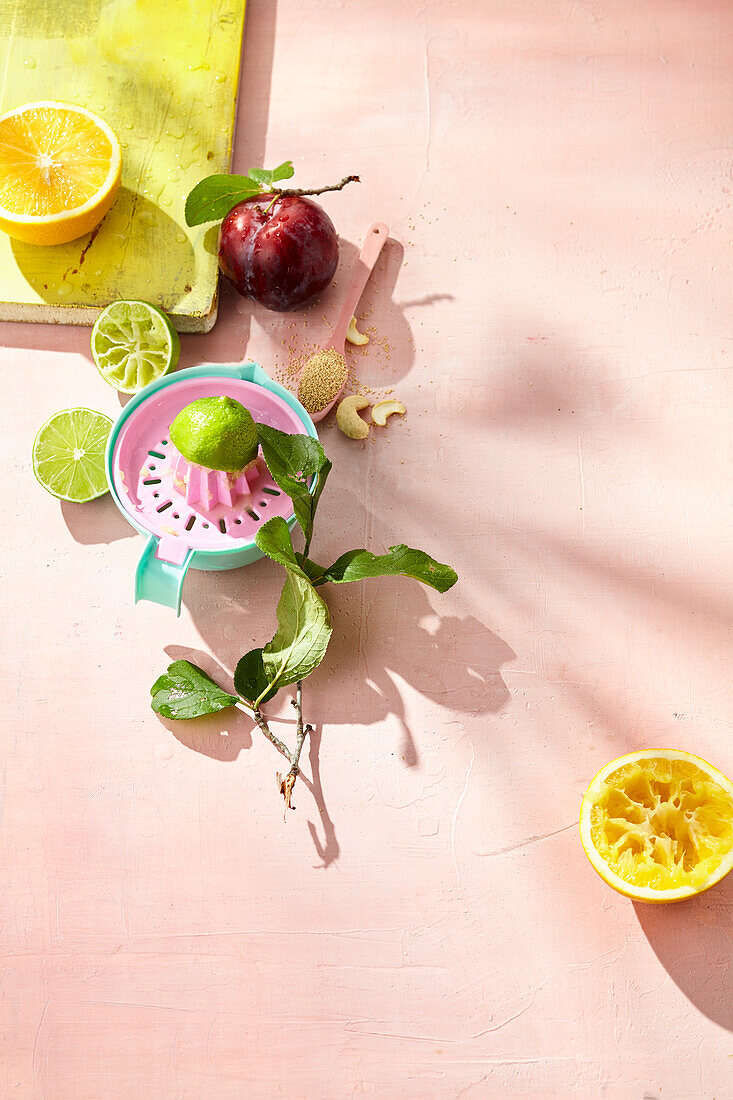 Citrus press with citrus fruits, red plum and cashew nuts on a pink background