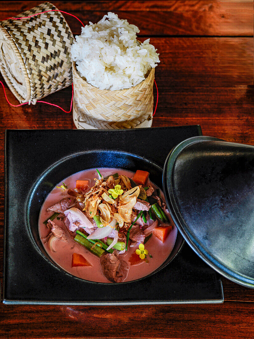 Laotisches Schweinefleisch-Curry mit gebratenem Knoblauch serviert mit Sticky Rice