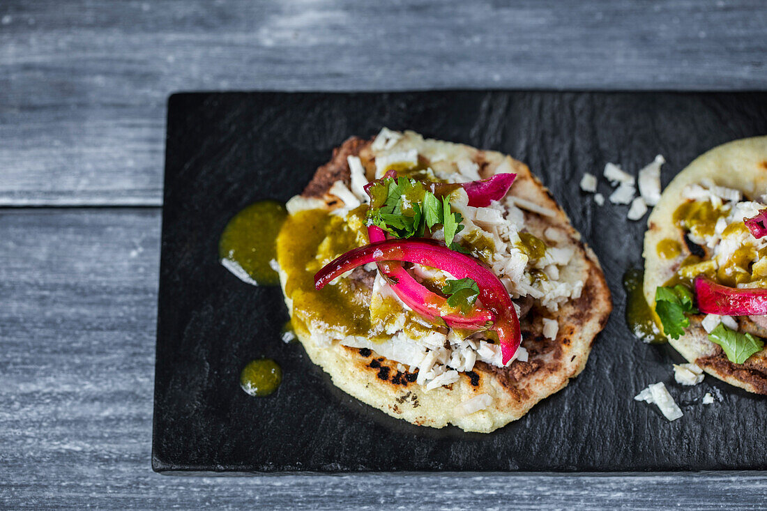 Yucatan panuchos with chicken and beans garnished with green sauce and pickled red onion