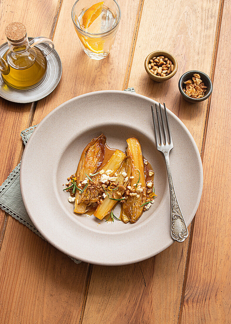 Top view of braised endives with orange juice on a wooden table next to a fork and different bowls