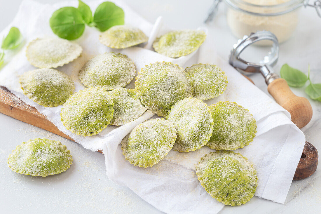 Fresh homemade ravioli with basil dough placed on napkin on wooden cutting board