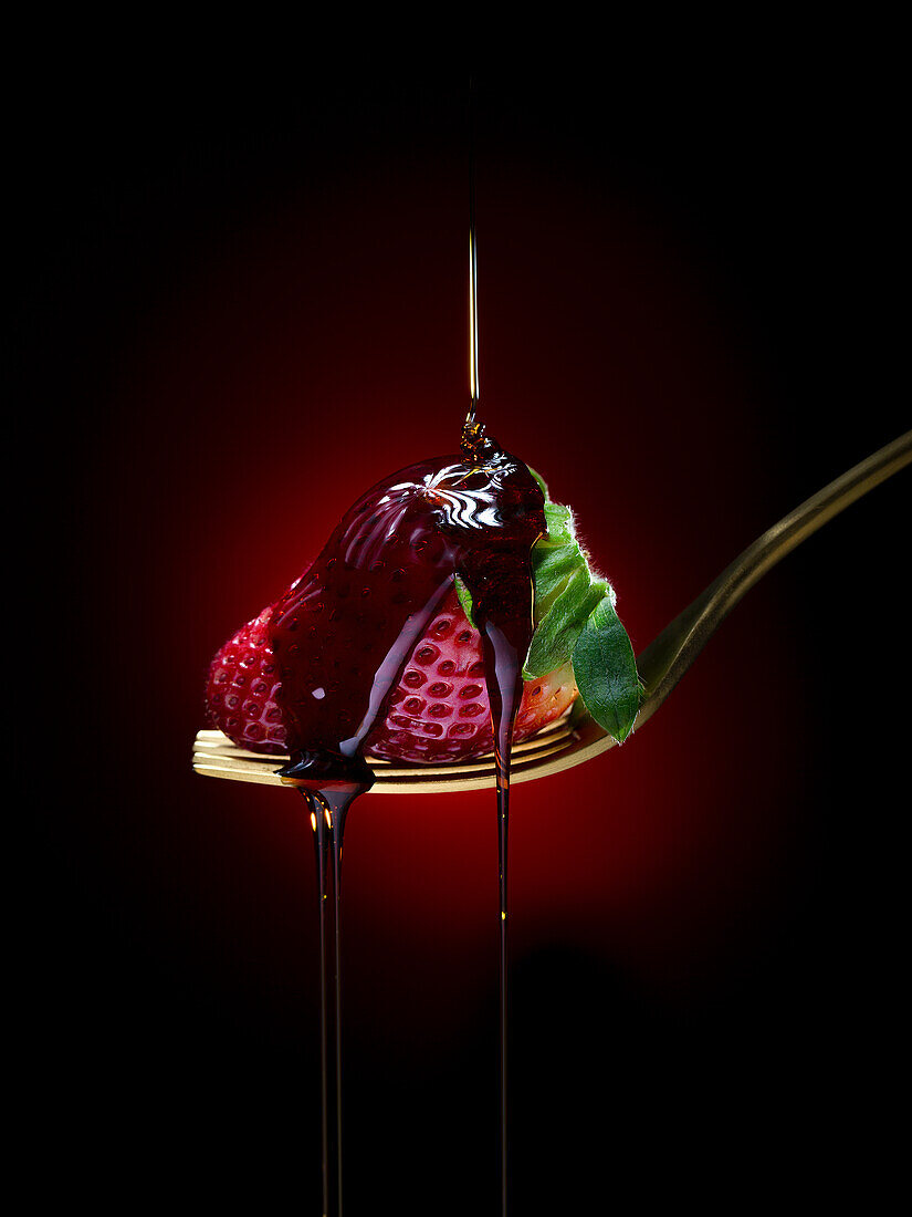 Sweet chocolate topping pouring on ripe red strawberry with green leaf on fork against dark background in studio with dim light