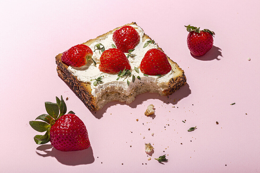 Top view of tasty nibbled toasts with cream cheese and ripe strawberries decorated with greens on pink background