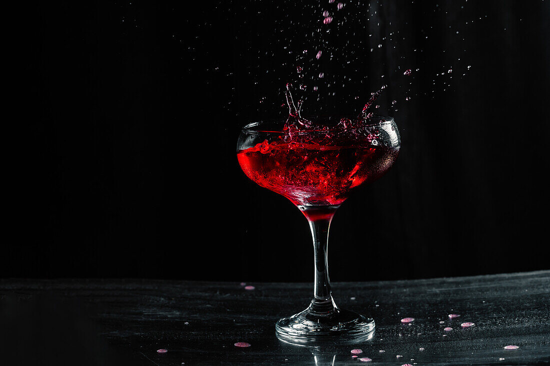 Splashing tasty alcoholic red wine with small drops in transparent wineglass placed on table against black background in modern studio