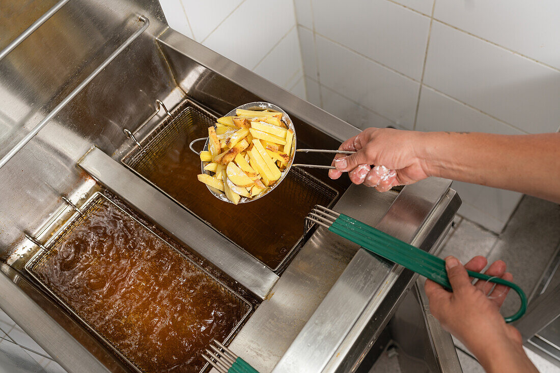 Pommes im Frittierkorb über heißem Ö in einer Großküche
