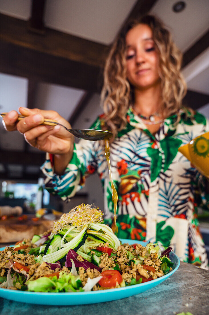 Frau beträufelt gesunden Gemüse-Quinoa-Salat mit Öl