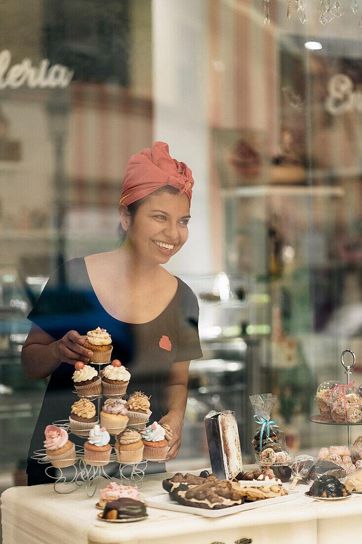 Frau mit Kopftuch richtet Cupcakes in einer Konditorei an