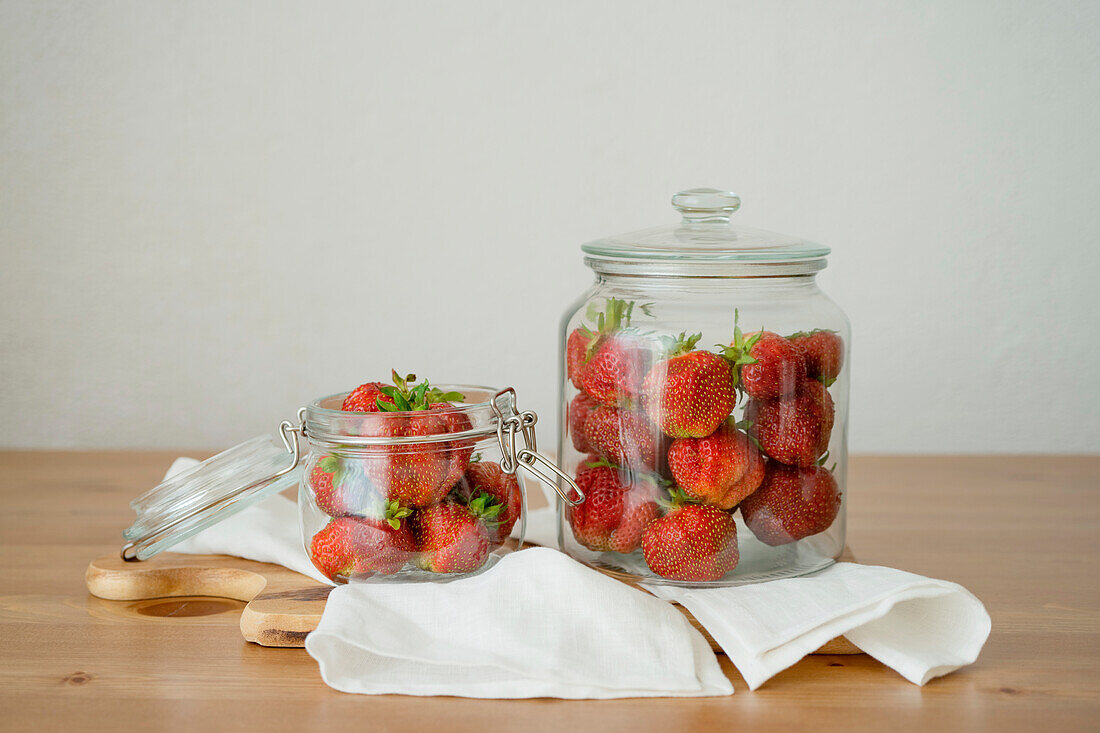 Fresh raw whole strawberries in glass jar placed on wooden cutting board on table in kitchen
