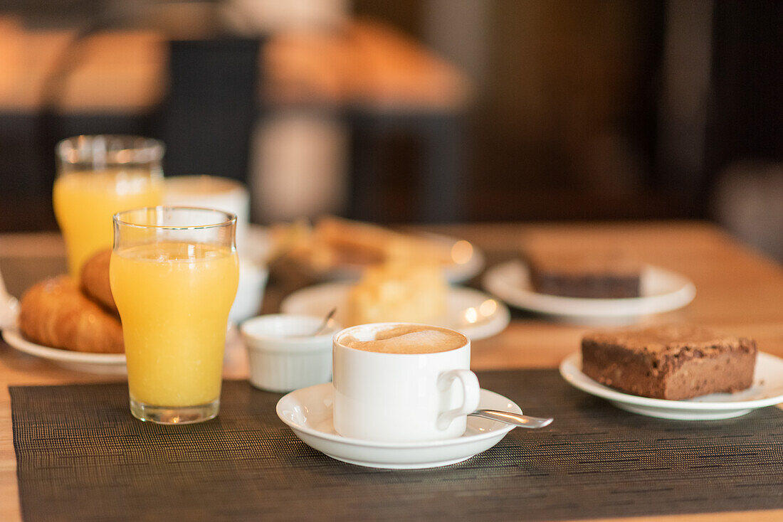 Fresh chocolate brownie near coffee in a mug and a glass of fresh orange juice during breakfast in restaurant