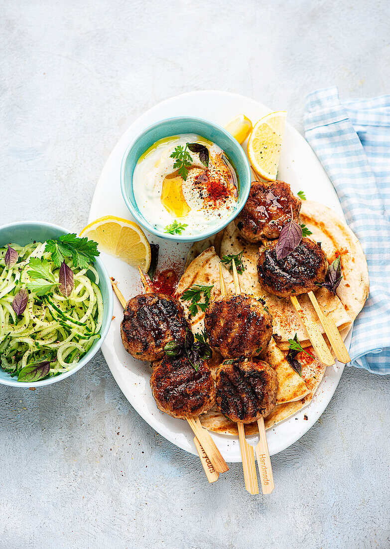 Meatballs on skewers with cucumber salad and dip