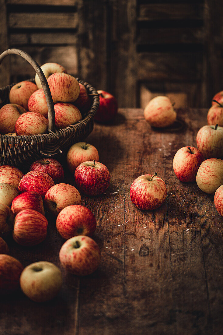 Äpfel in Weidenkorb und auf rustikalem Holztisch