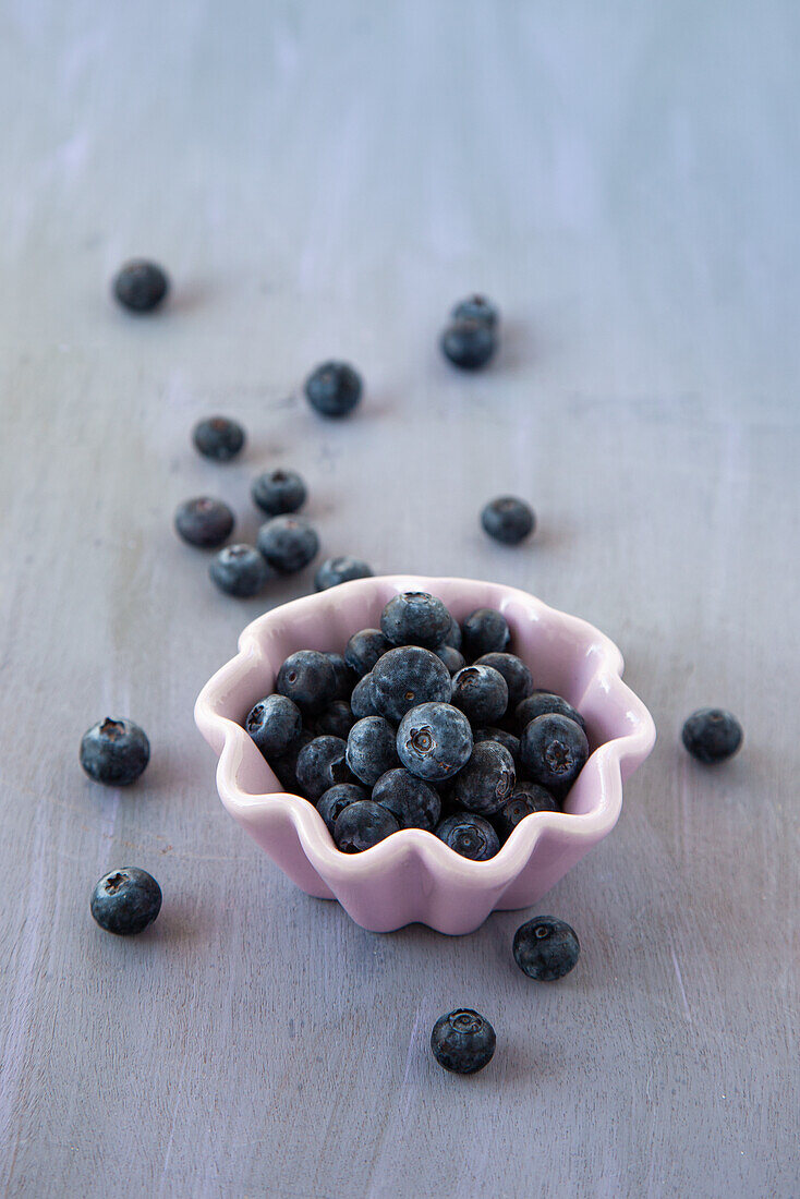 Blueberries in a small bowl and on a grey background