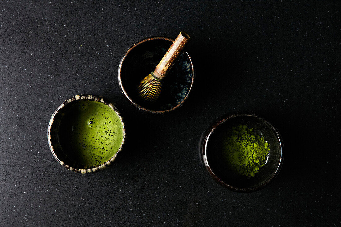 Matcha tea with matcha whisk and tea powder in small bowls on a dark background