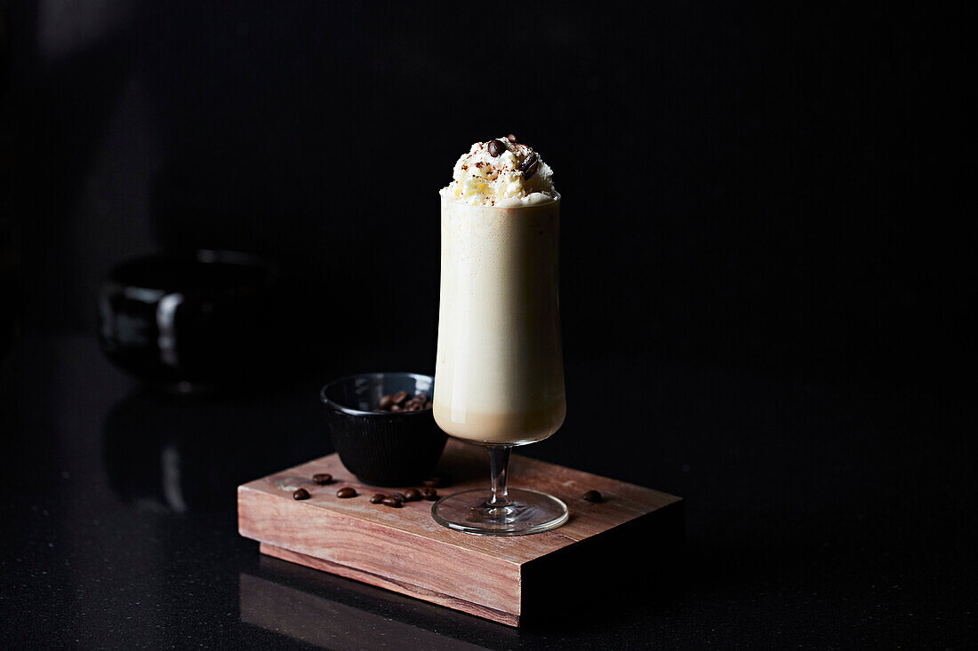 Coffee latte with whipped cream in a glass on a wooden platter