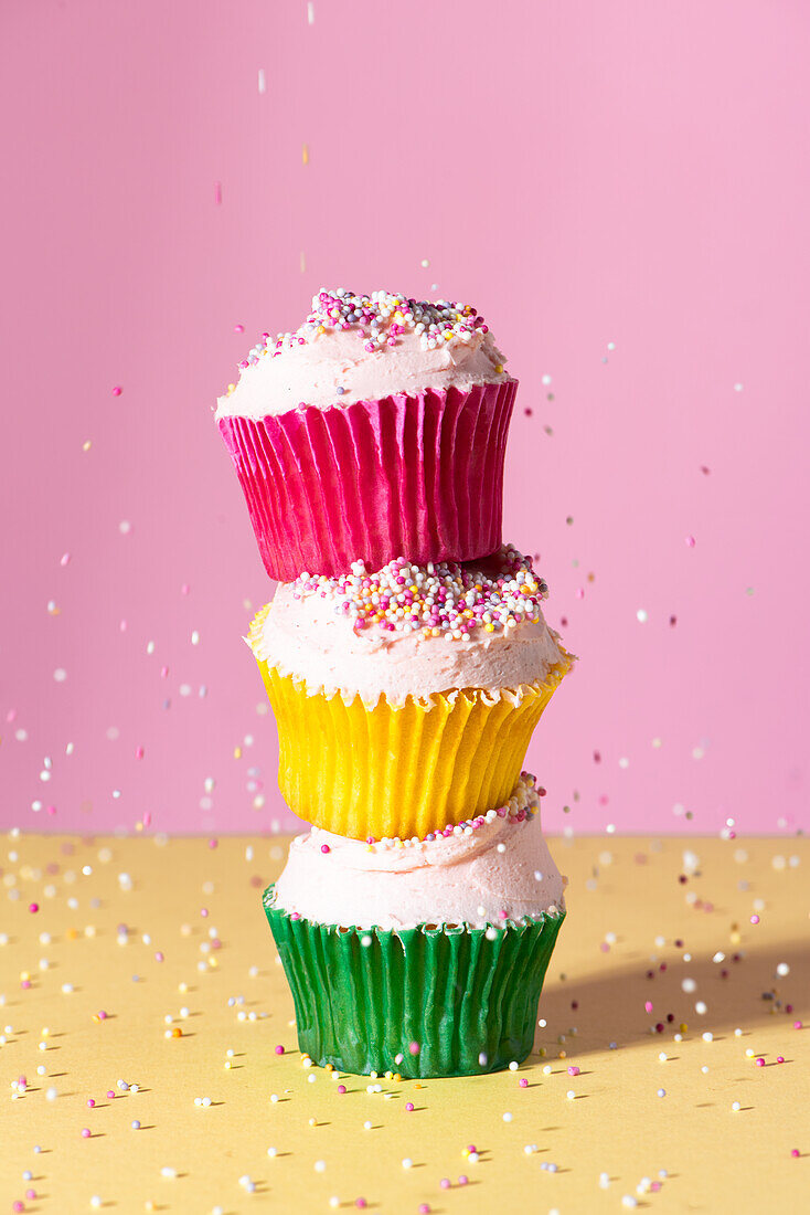 Drei Cupcakes mit Buttercreme und Streuseln in verschiedenfarbigen Papierförmchen