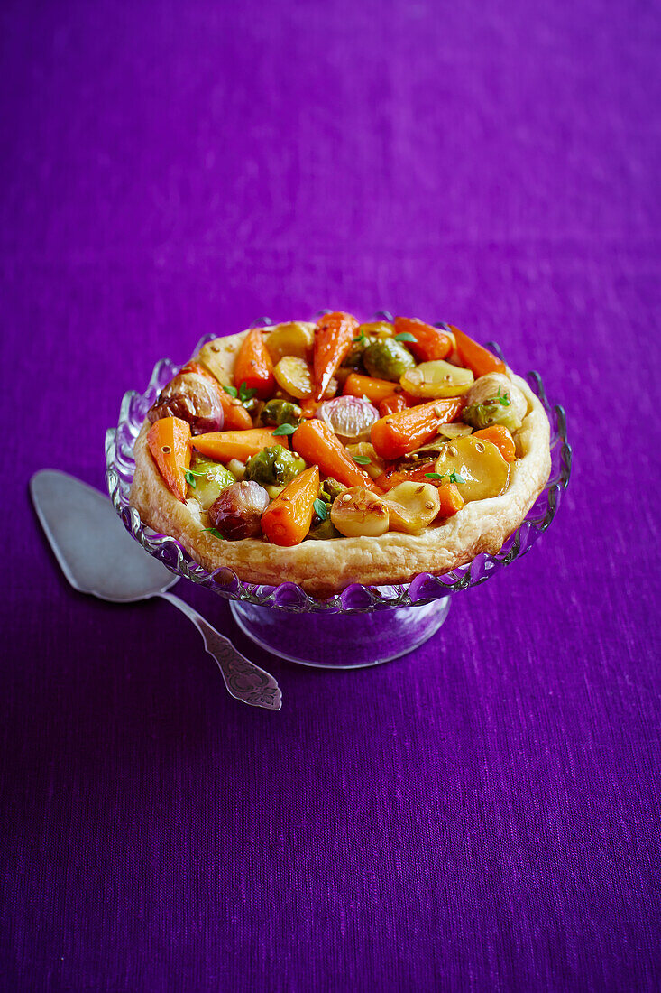 Puff pastry vegetable pie on pastry stand and purple background