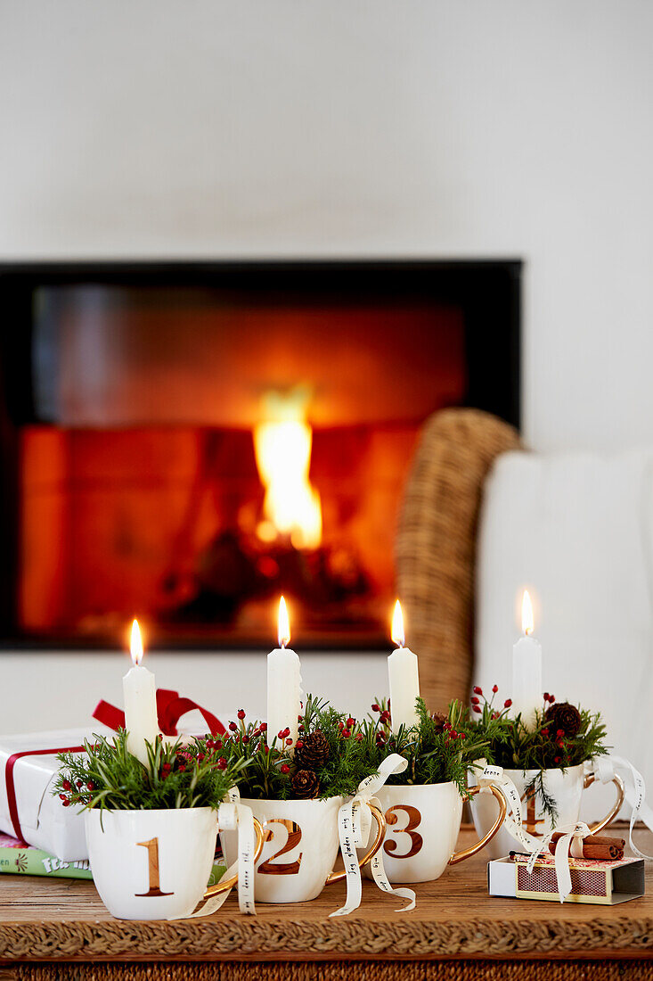 Advent candles in numbered cups stuffed with leaves and berries in front of fireplace