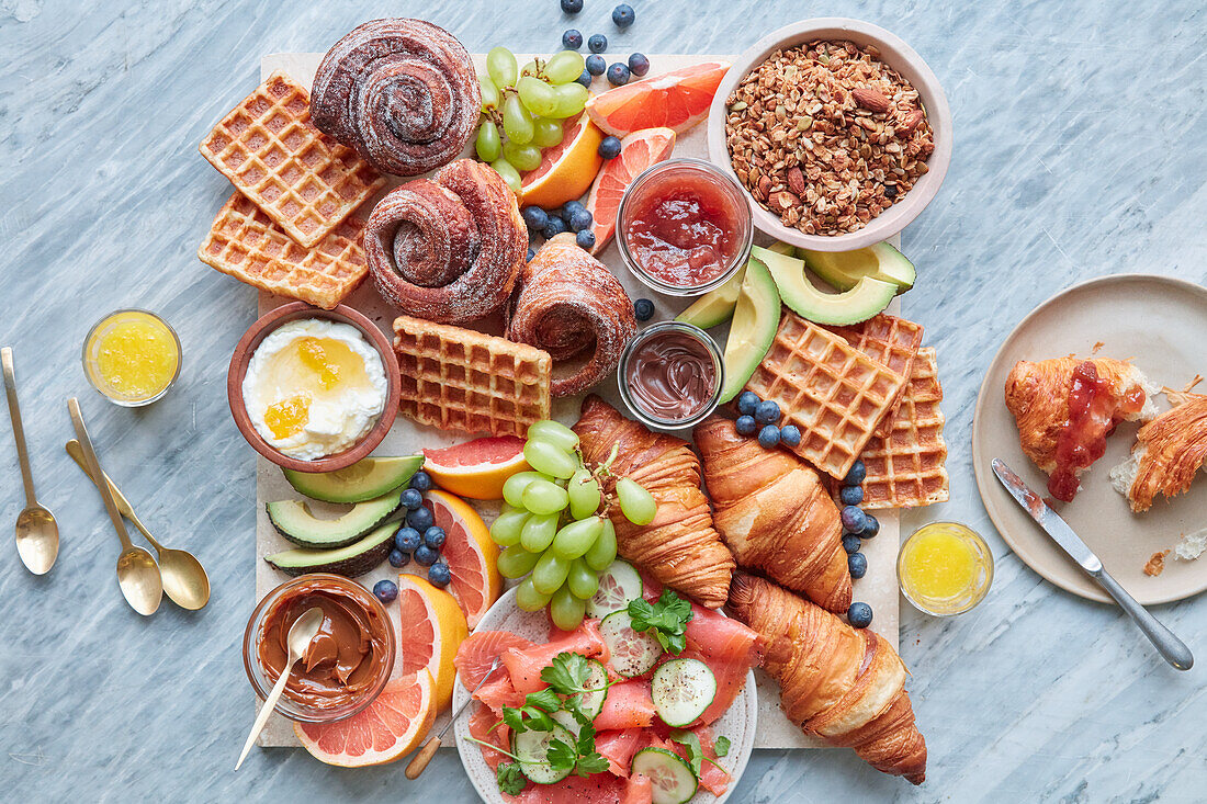 Frühstücksplatte mit Zimtschnecken, Croissants, Waffeln, Lachs und Obst