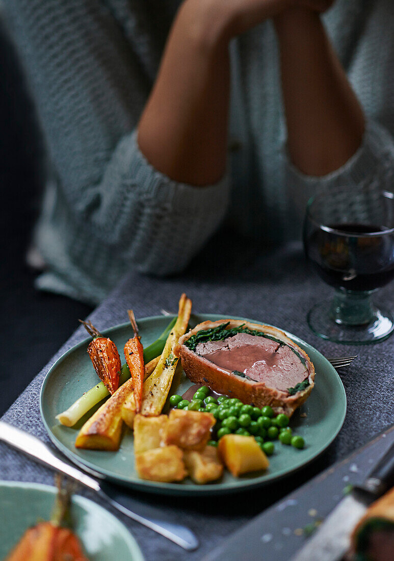 Beef Wellington wrapped in spinach and bacon and served with roasted root vegetables and peas