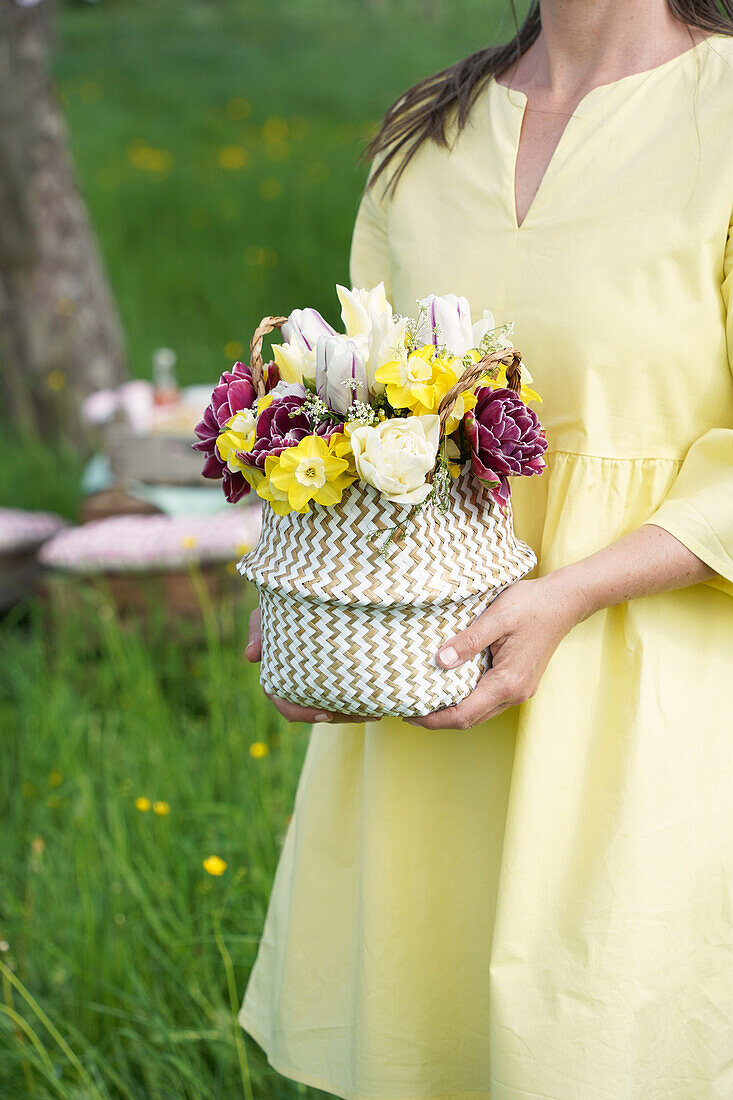 Geflochtener Korb mit Frühlingsblumen in den Händen einer Frau im Garten