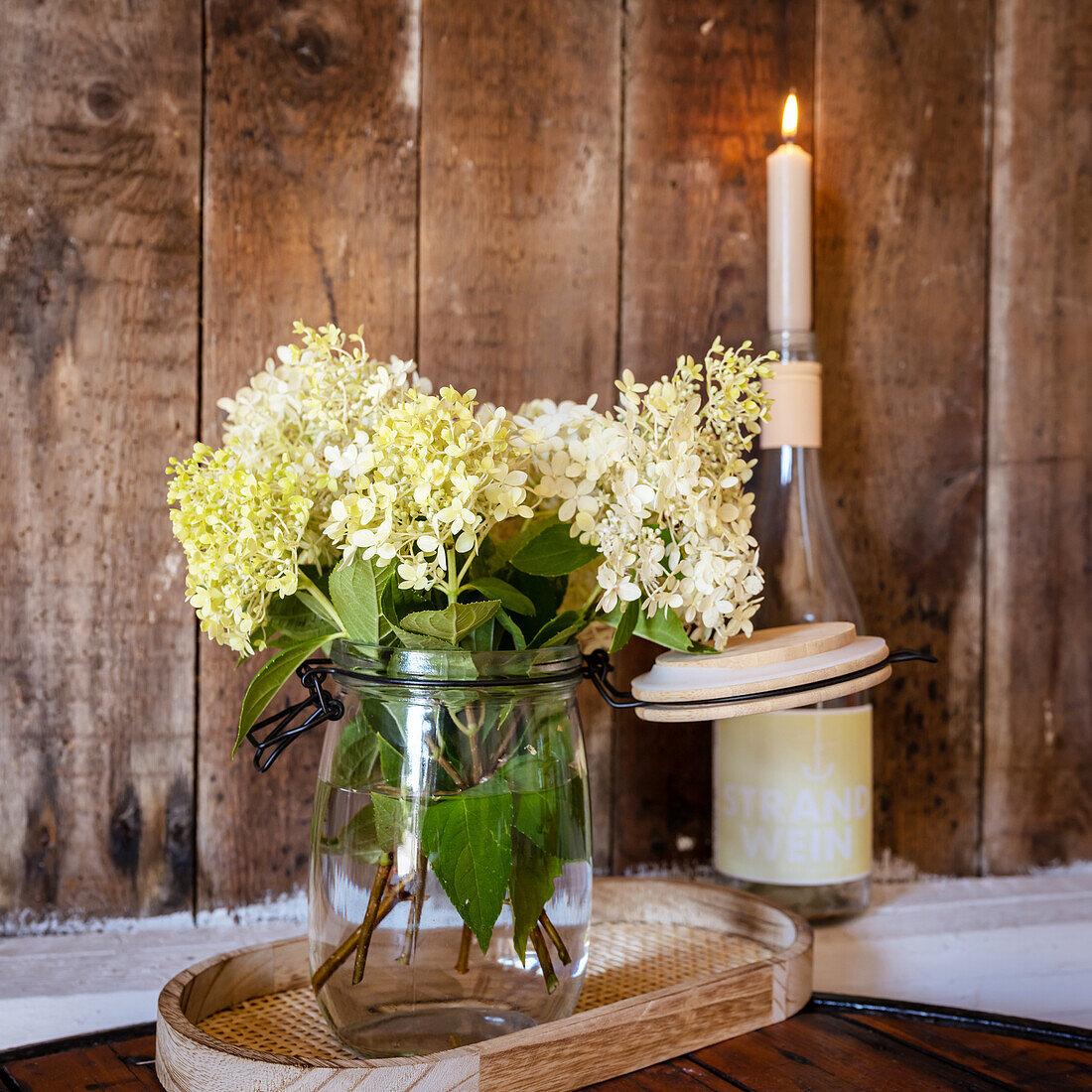 White hydrangeas in a vase and a candle in a wine bottle in the background