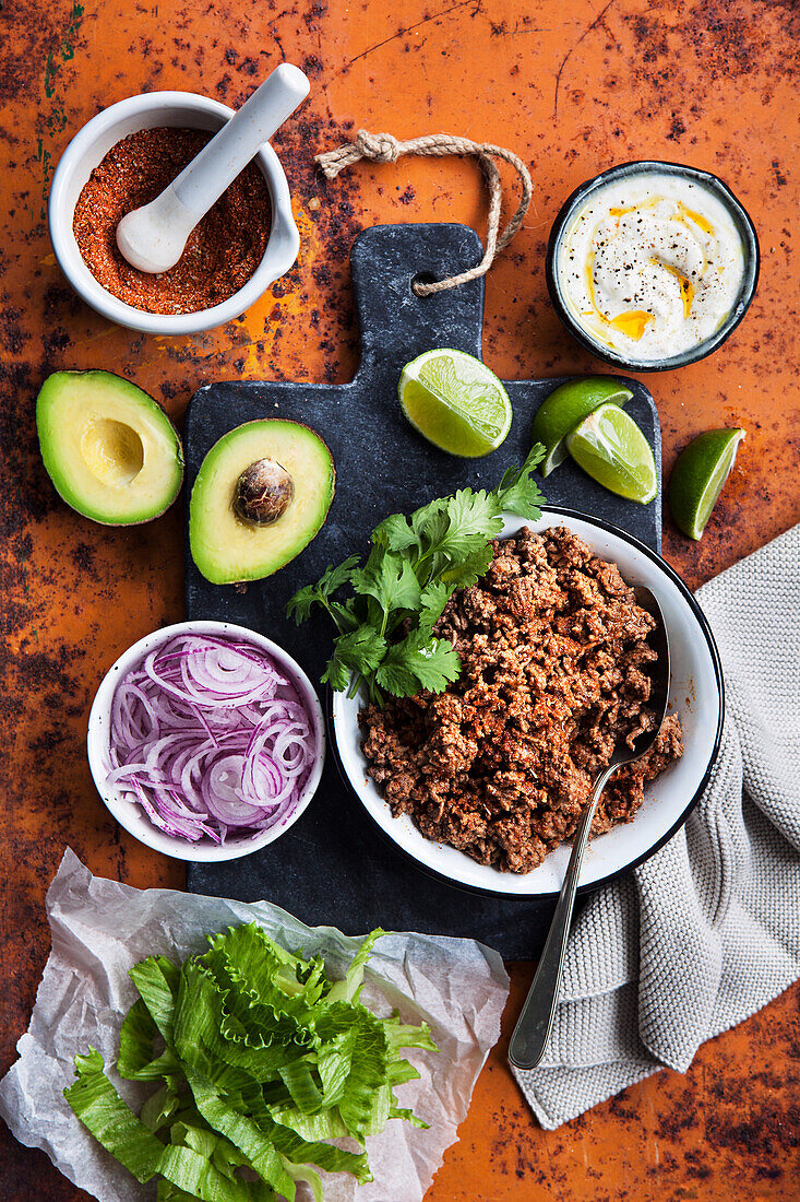 Zutaten für Tacos: Hackfleisch, Zwiebeln, Salat, Limetten, Koriander und Avocado