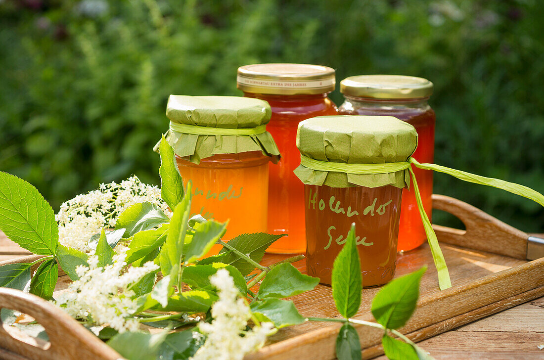 Elderberry jelly and elderberry blossom on a tray on a wooden table in the garden