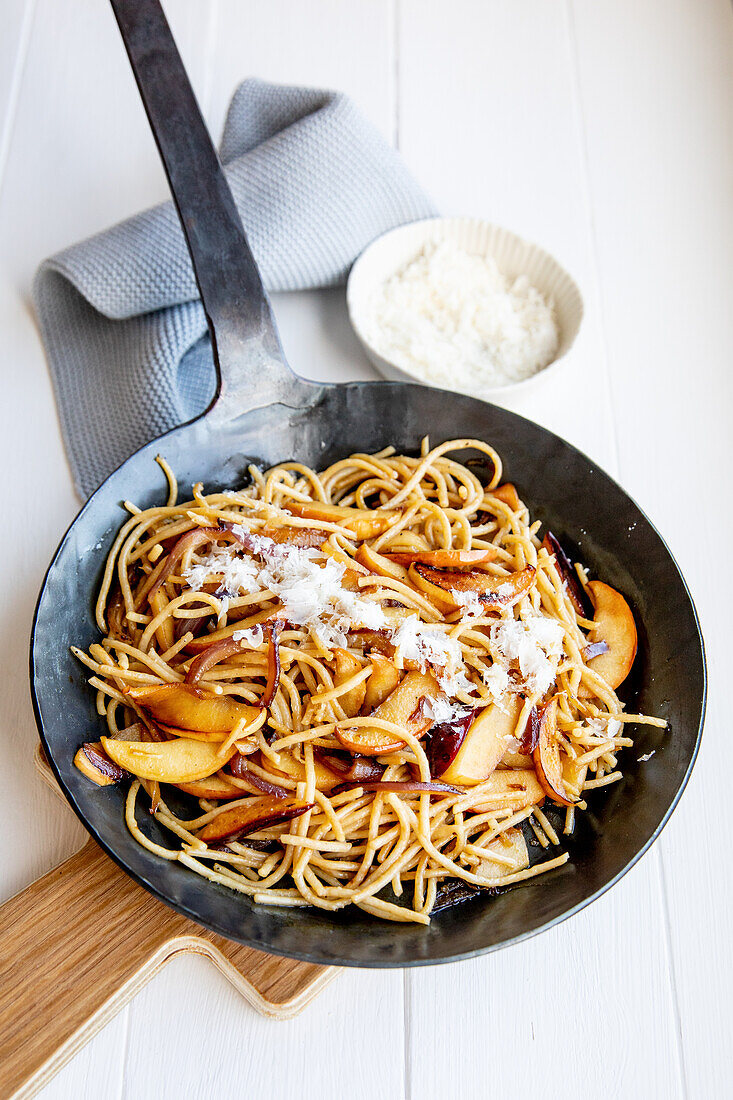 Wheat pasta in a pan with onions and apples