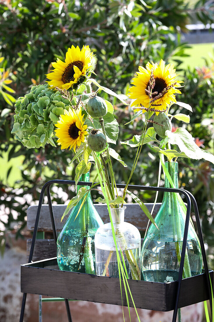 Strauß aus Sonnenblumen und Mohnkapseln in Milchkannen