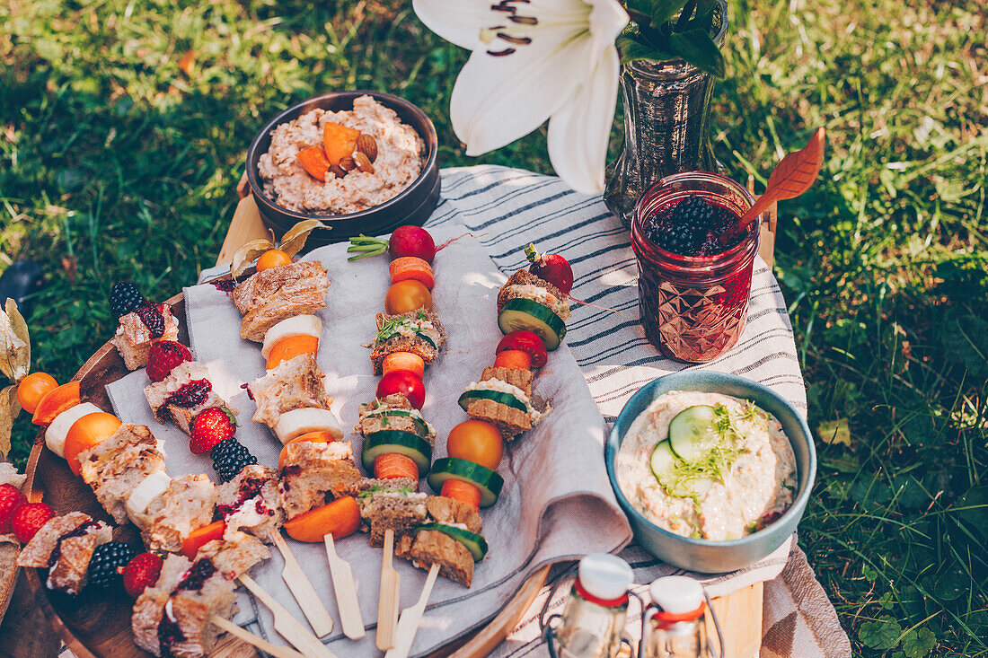 Picknick im Garten mit vegetarischen Sandwich-Spießen, Früchten und Aufstrichen