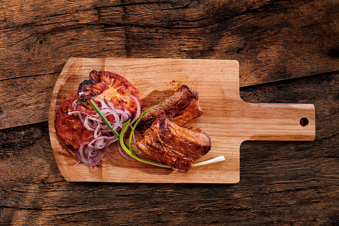Spareribs with grilled tomato slices on a wooden board